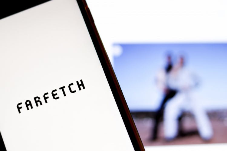 Farfetch logo on smartphone screen in front of the brand website