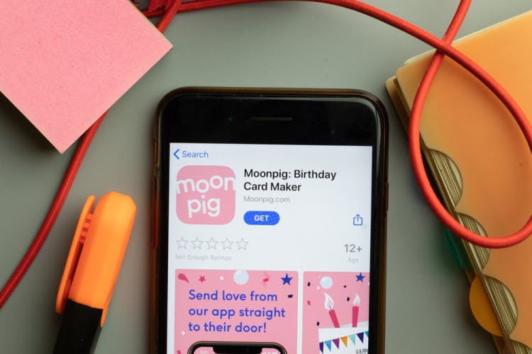 A phone screen displaying the Moonpig app with a marker pen and a binder arranged around it.