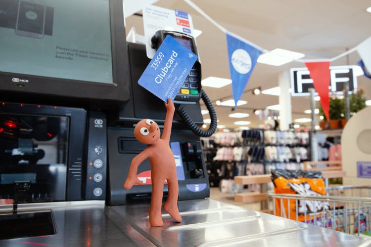 Morph holding a Tesco Clubcard to card reader at self-service checkout in Tesco supermarket in Prices That Take You Back campaign