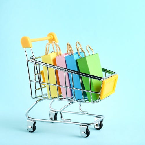miniature shopping basket containing four paper shopping bags of different colours upon light blue background