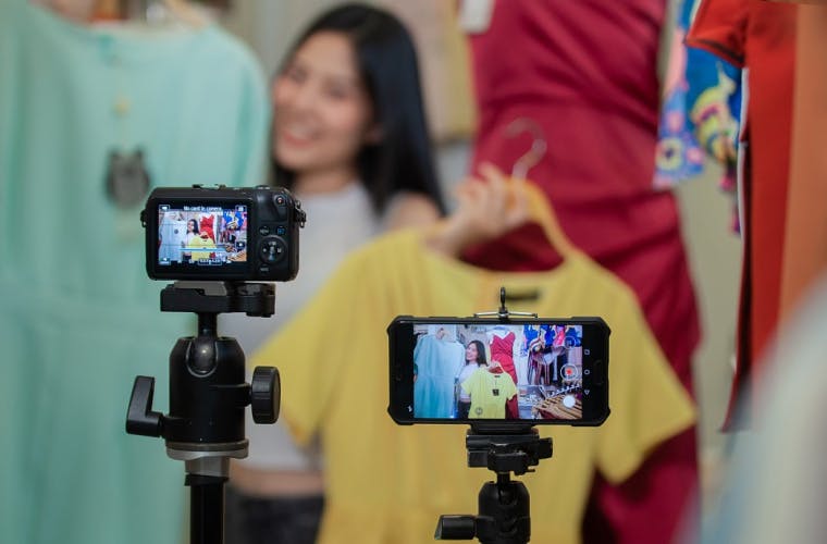 Woman showing off clothes to a camera and smartphone as she livestreams.