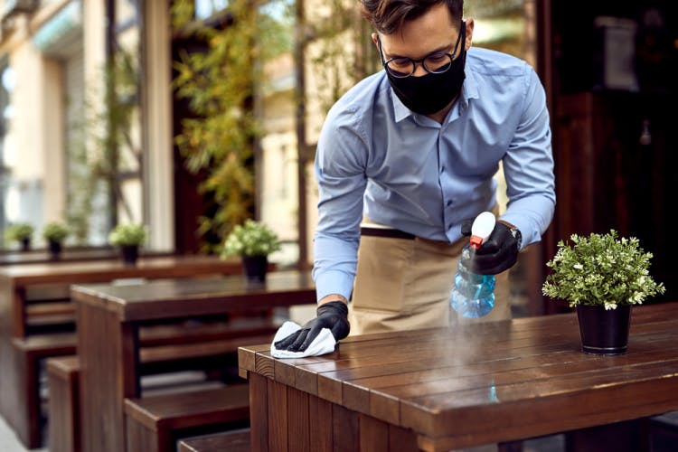 man in mask cleaning restaurant table