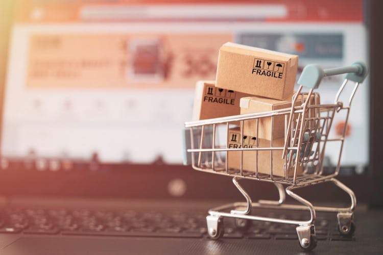 Stock photograph of a miniature shopping card with packages resting atop a laptop keyboard.