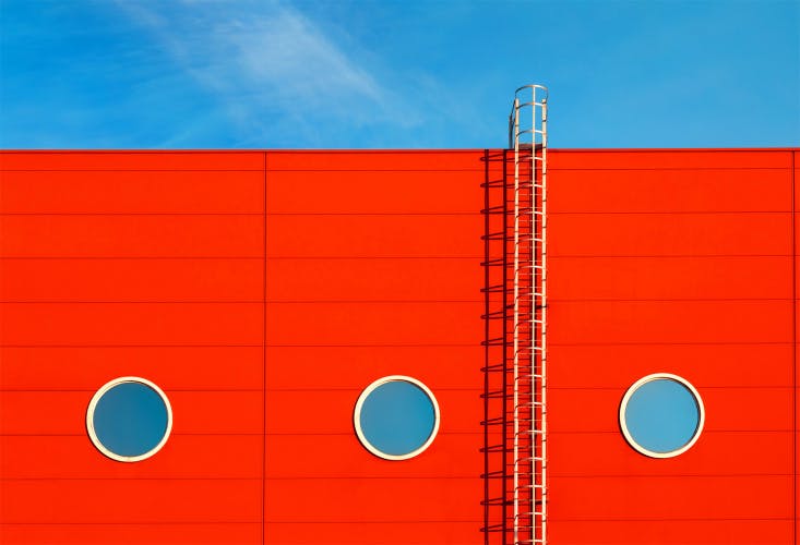 white ladder on red background-with port holes on blue sky
